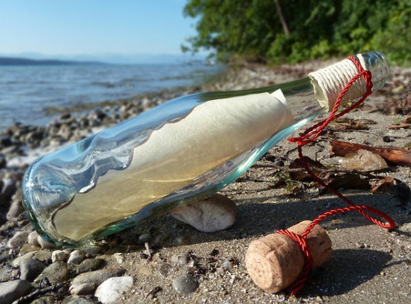 Glass bottle with rolled letter on a beach, symbolizing spiritual messages, emotional healing, and creative self-expression found through nature.
