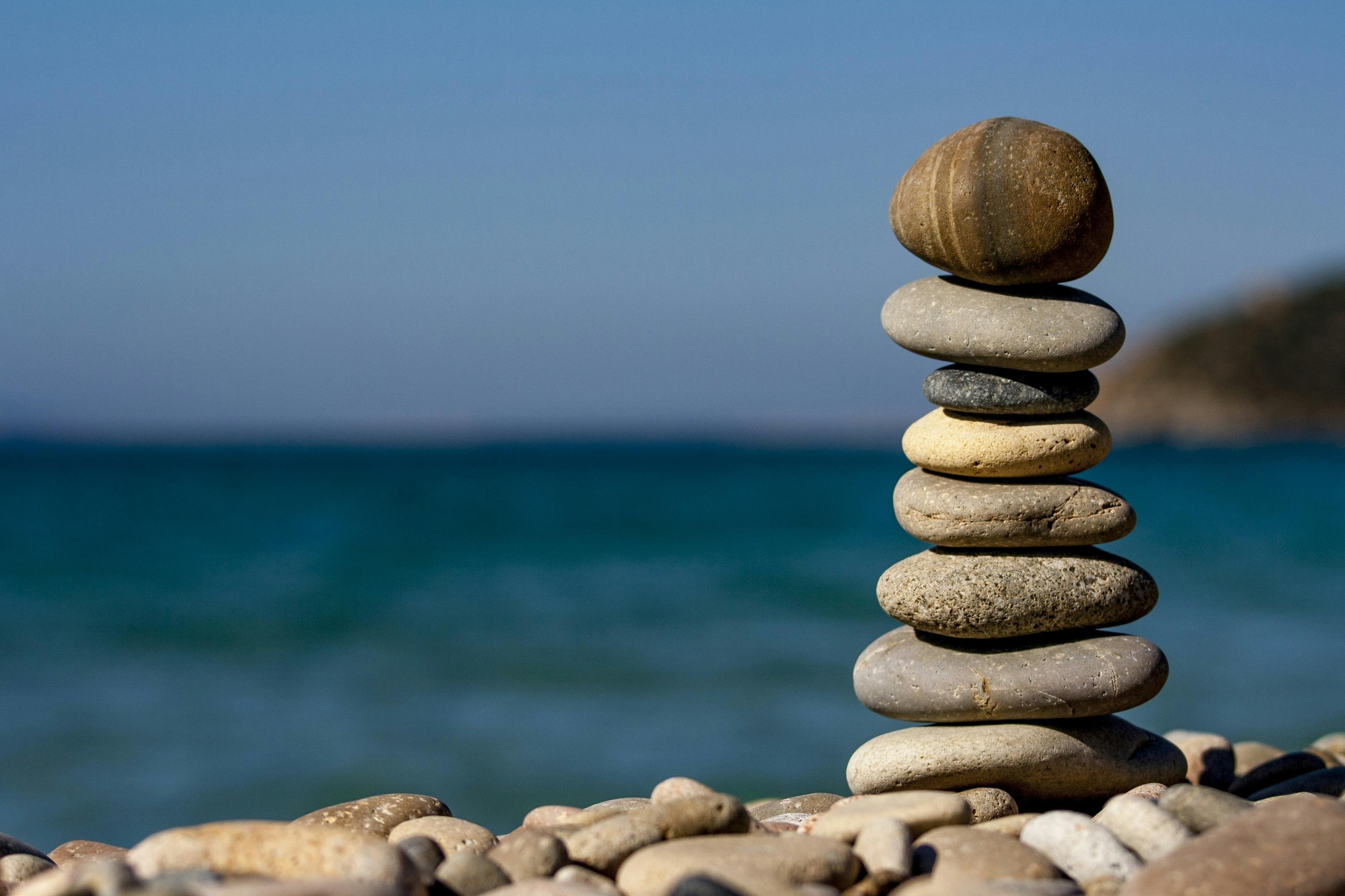 Zen rock stack on the beach with blue ocean in the background, representing emotional balance, mindfulness, and spiritual grounding.