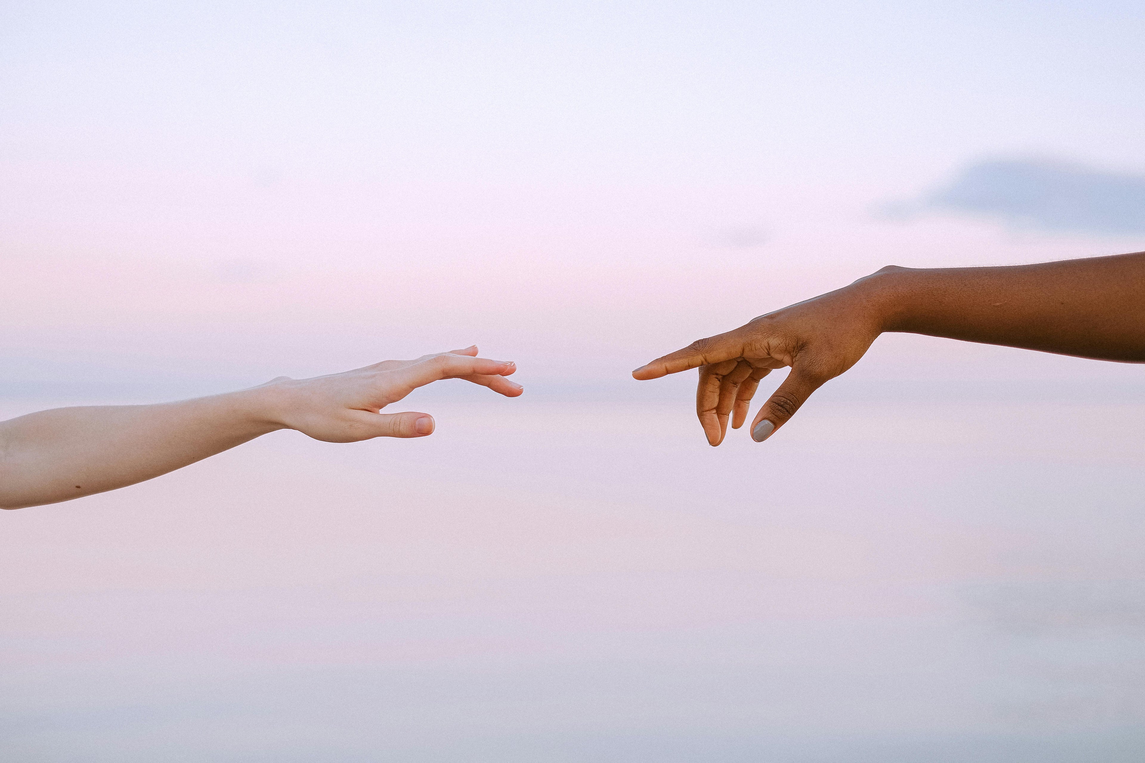 Diverse hands reaching toward each other at sunset, representing emotional connection, spiritual healing, and creative love across difference